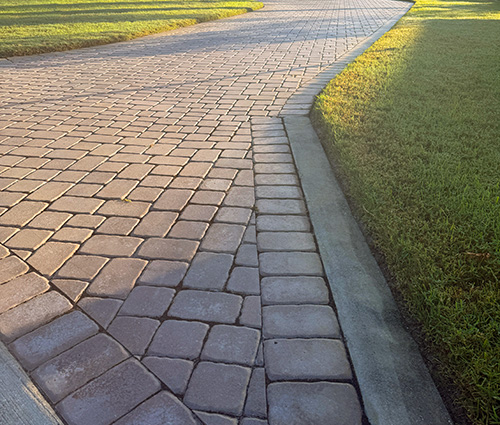 A curved stone pathway bordered by grass, showcasing a pattern of paving stones under natural light.